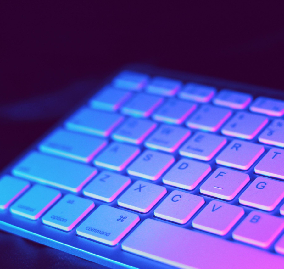 Close-up of a modern keyboard illuminated with vibrant purple and blue neon lighting.
